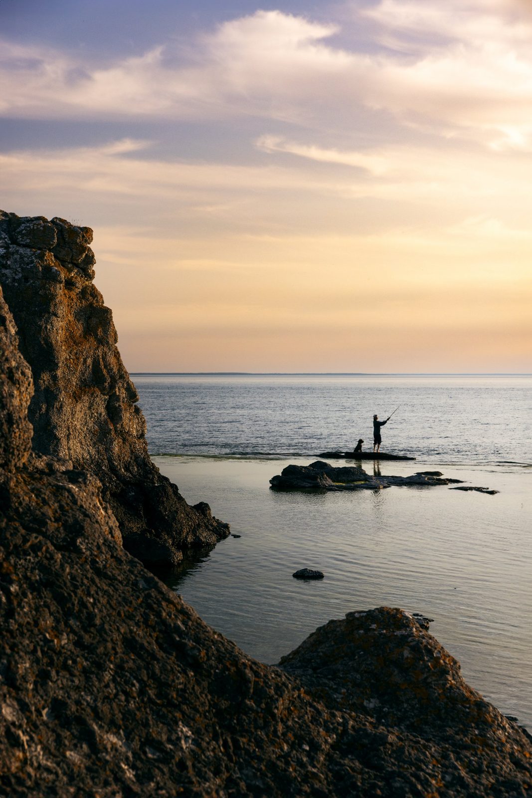 Fisherman and dog on a rock at sunset