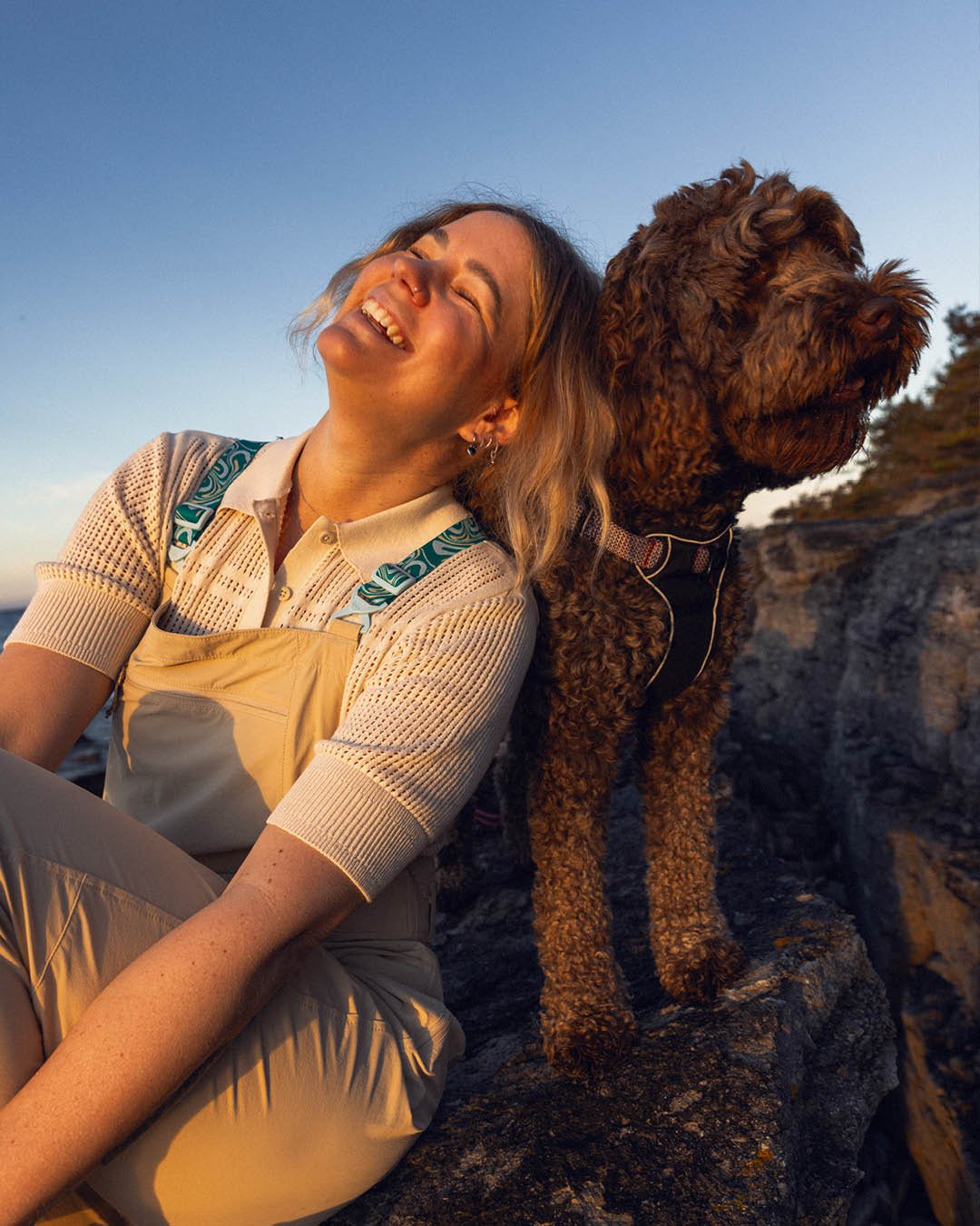 Laughing woman with a dog on a rock at sunset