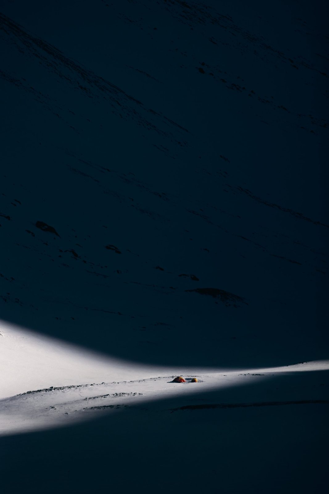 Tents in a strip of sunlight on a dark slope